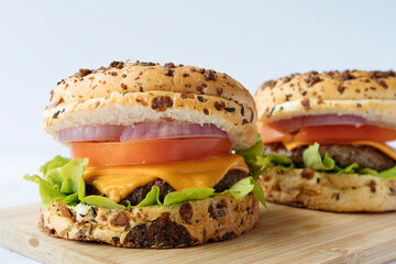 Two delicious hamburger with cheese, tomato and vegetables on a wooden board