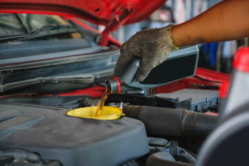 Car mechanic working in the local garage by pouring new oil into the engine. Oil change of car maintenance services.