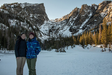 Lesbian couple standing in front of Dream Lake in Rocky Mountain National Park in Colorado. The peaks are covered in snow and the lake is frozen over