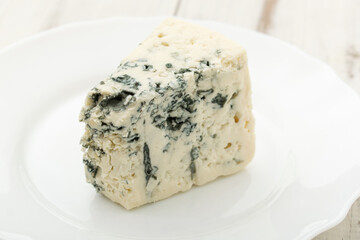 Blue cheese on a white plate on a wooden background.