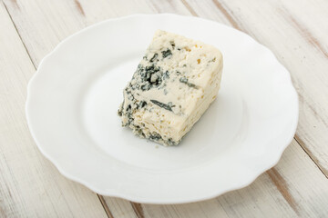 Blue cheese on a white plate on a wooden background.