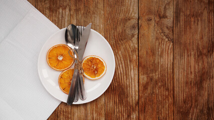 Overhead view of fall Thanksgiving or Christmas table setting over wooden table with copy space. White plate with dry oranges