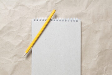  Gray notepad with white coiled spring and pencil on a background of beige crumpled craft paper