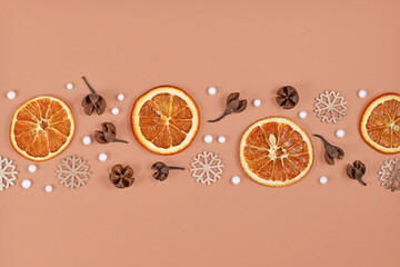 Seasonal winter flat lay with dried orange slices, fruit husks and wooden snowflake ornaments in a row on cream colored background