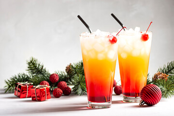 Two alcoholic cocktails Sunrise with tequila stand near fir branches on a gray background, horizontal orientation, copy space, selective focus