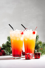 Two alcoholic cocktails Sunrise with tequila stand near fir branches on a gray background, vertical orientation, copy space, selective focus