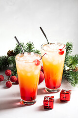 Two New Year's cocktails of tequila Sunrise on a gray concrete background, next to fir branches and New Year's decorations. Vertical orientation, selective focus, copy space.