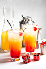 Two festive cocktails of tequila Sunrise on a gray concrete background, next to boxes with gifts. Vertical orientation, selective focus.