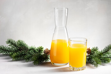 Orange juice in a glass stands next to the decanter against the background of spruce branches.