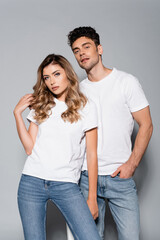  couple in white t-shirts and jeans posing isolated on grey