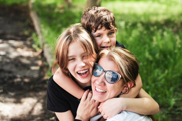 Happy mother surrounded by her children of different ages, a teenage daughter and a young son hugging their mother and having fun and talking together