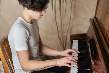 At home, a teenage boy plays the piano and relaxes playing with pleasure forgotten melodies. The guy is honing his skills every day playing the piano © Мар'ян Філь