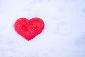 Red plush heart, lying in winter on the white pure snow in the sun. Love the concept of Valentine's Day. Lost heart top view. Valentine's day background with space to copy.