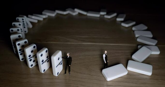 Two drawn businessmen drop and stop white dominoes on wooden background.