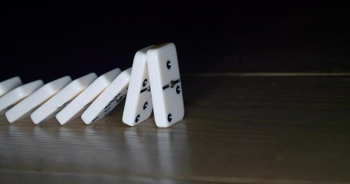 White dominoes falling down on wooden background. The last tile doesn&rsquo;t fall. Concept of domino effect, chain reaction, risk management.