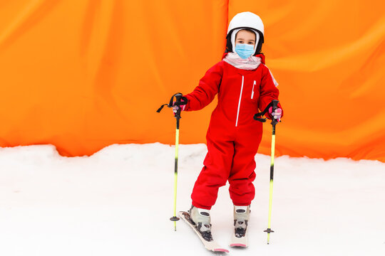 Portrait of a little girl skier in medical mask during COVID-19 coronavirus on a snowy mountain at a ski resort