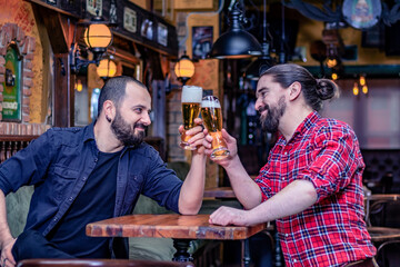 Two male friends drinking at the pub. They are laughing and toasting with tall glasses full of beer. Cheers.