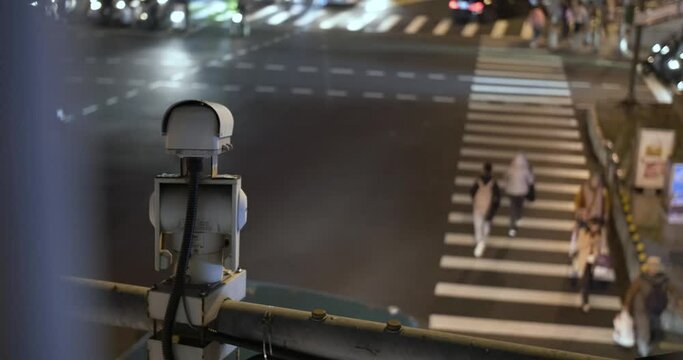 A security CCTV camera at pedestrian crossing on busy street at night.  People walking across an intersection and cars driving by. Government surveillance in Taipei city, Taiwan, Republic of China.