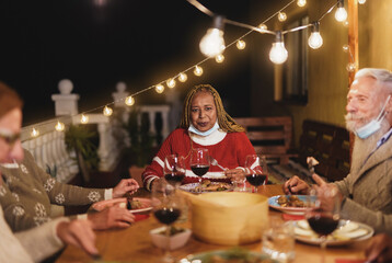 Multiracial senior people celebrate christmas together and enjoy dinner outdoor while wearing surgical face mask for coronavirus