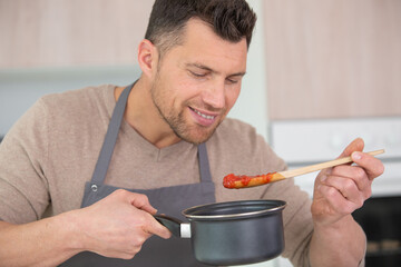 male cook tries hot pasta sauce from pan