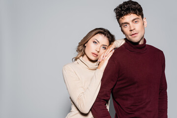 Fototapeta premium young couple in turtleneck jumpers embracing isolated on grey