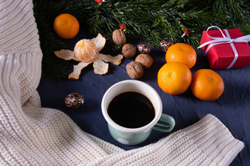 fir branches on the table near tangerines, warm sweater, coffee mug and nuts