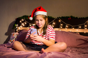 New Year girl in the evening, in a New Year's hat with a phone in her hands, sits on the bed © irinad85