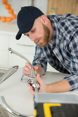 young plumber installing tap in a kitchen