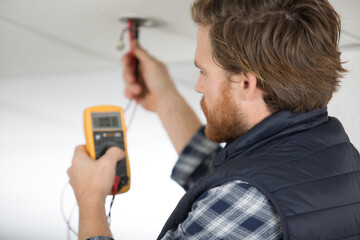 electrician measuring voltage from wire on the ceiling