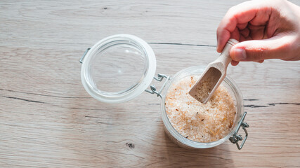bath salt in glass with male hand on wooden table