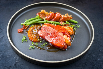 Modern style minimalistic gourmet duck breast filet with beans and bacon in orange sauce offered as close-up on a Nordic design plate