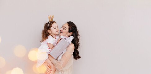 Happy family - mom and daughter on a beige background. Beautiful woman holding a little girl with a gift. christmas and new year concept