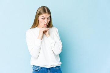 Young blonde woman isolated on blue background praying for luck, amazed and opening mouth looking to front.