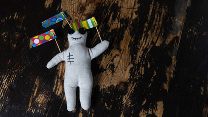 Close-up of a voodoo doll with straight pins and strange flags on dark wooden background. Mystic concept.