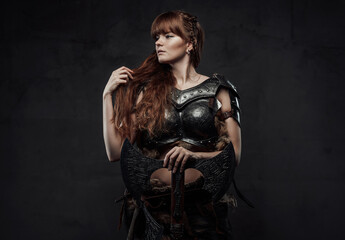 Fototapeta na wymiar Beautiful northern amazon in dark armour with huge axe posing in dark background.