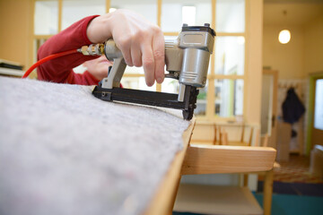 Hand working with pneumatic stapler. Old armchair restoring. Nonwoven upholstery material. Woman...