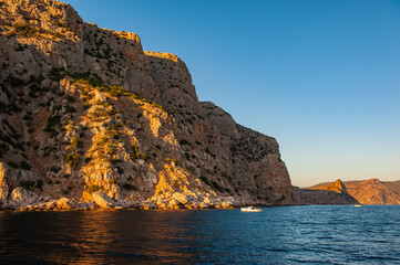 pleasure boat with tourists in the sea against the backdrop of rocks at sunset.