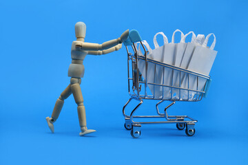Wooden man carrying Shopping cart with medical protective bandage on a blue background.
