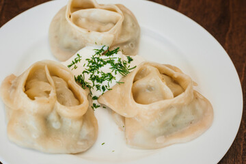 Large manti on a white dish with sour cream and herbs. Eastern cuisine. Meat in dough. Stands on a wooden table