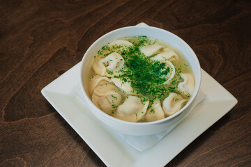 Dumplings with meat in broth with herbs in a white plate on a dark background. Russian folk cuisine. White bowl on a wooden table.