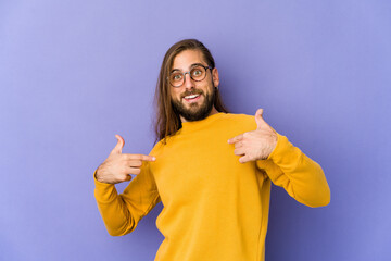 Young man with long hair look surprised pointing with finger, smiling broadly.