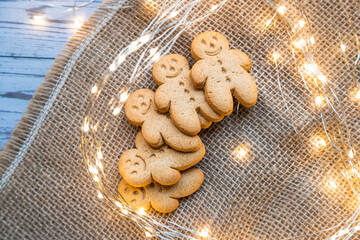 a stack of gingerbread cookies or ginger-man on a white table on brown canvas with Christmas lights - 396639380