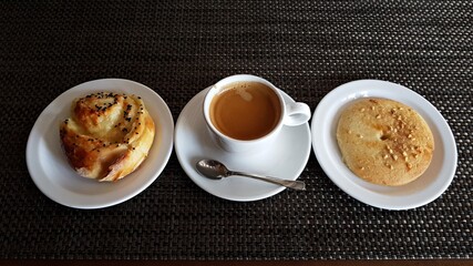 Cup of black coffee with cookies and a bun on plates
