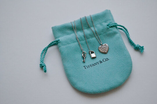 Moscow, Russia, November 2019: Signature Tiffany and Co. Branded packaging jewelry: soft turquoise bag with sterling silver key, lock and heart on the chain. White background. Copy space