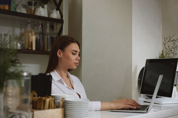 A young woman works in a laptop behind a bar