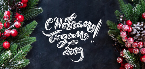 Happy New Year text in russian, hand lettering inscription with red balls, tree branches and cones on a dark background. Christmas greeting card.