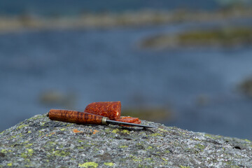 Knife cutting sausage in the mountain with blurry mountain landscape in background.  Outdoor food.