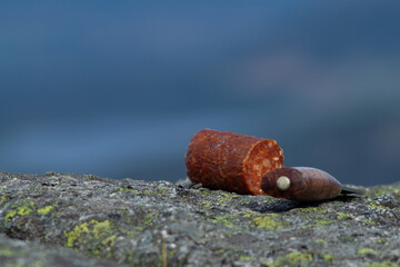 Knife cutting sausage in the mountain with blurry mountain landscape in background.  Outdoor food.