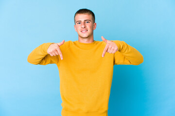 Young caucasian handsome man points down with fingers, positive feeling.