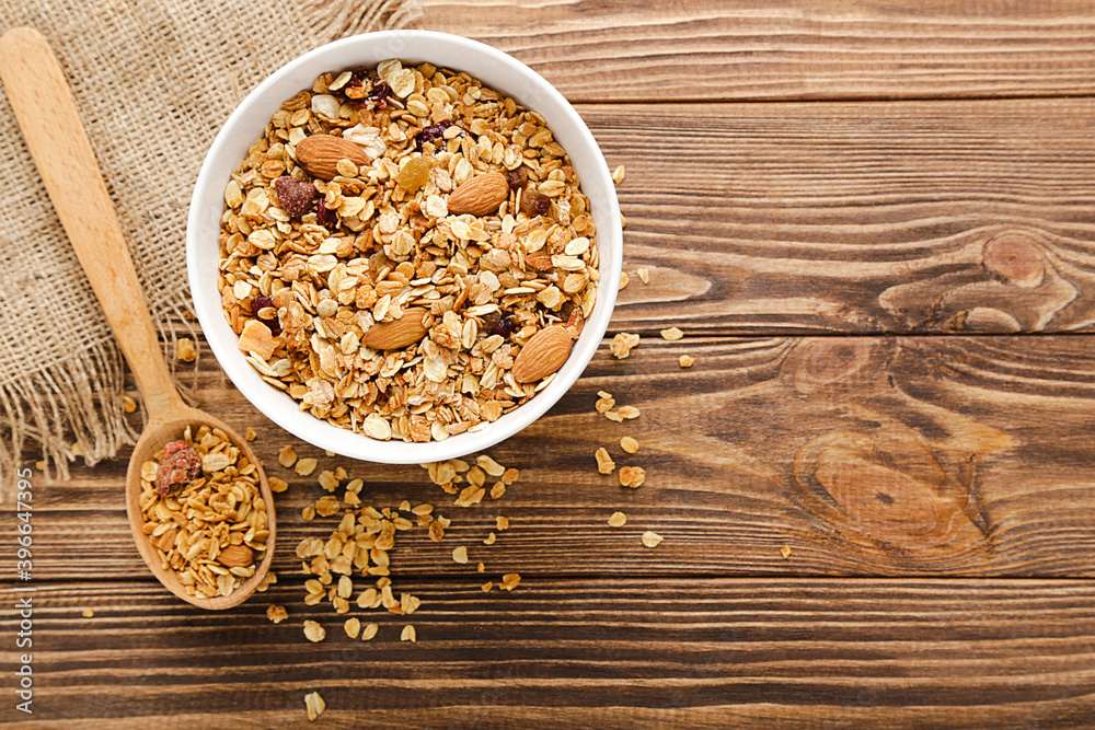 Poster Tasty granola in bowl and spoon on brown wooden background